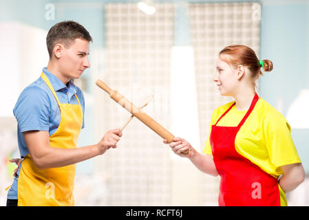 man and woman in an apron with kitchen utensils fighting in the kitchen Stock Photo