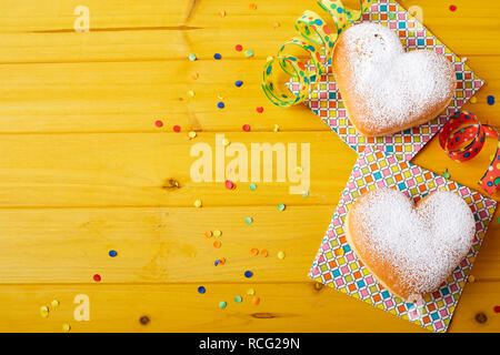 Two heart-shaped cookies with decorations of ribbons and confetti on yellow wooden surface with copy space. Easter treats concept Stock Photo
