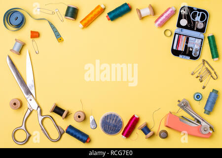 Composition with threads and sewing accessories - scissors, centimeter, pins on yellow background. Stock Photo