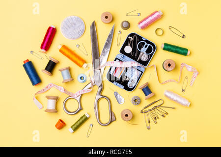 Composition with threads and sewing accessories - scissors, centimeter, pins on yellow background. Stock Photo