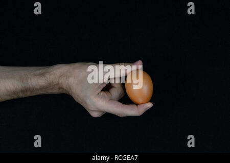Man holding a brown egg with his fingers on a black felt background Stock Photo