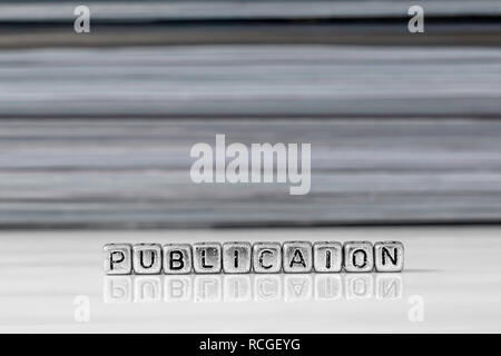 Publication on beads with magazines stacked in the background reflected on a white surface Stock Photo