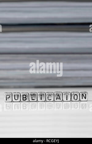 Publication on beads with magazines stacked in the background reflected on a white surface Stock Photo
