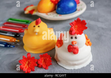 Multi-colored Easter eggs lie next to paint for coloring and marzipan Easter cakes in the shape of chickens. Stock Photo
