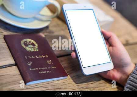 Woman holding a smartphone with a chinese passeport and coffee cup on a wooden table Stock Photo