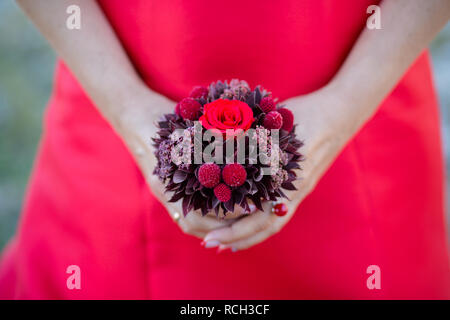 A shot of an unrecognizable woman in a red dress holding a red bouquet of flowers in front of her Stock Photo