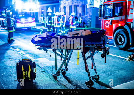 Eine Trage für Verletzte und ein Rucksack von Rettungskräften steht während eines Brandes vor einem Mehrfamilienhaus. Stock Photo