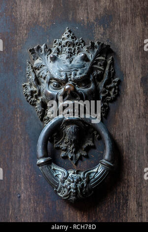 Devil's head bronze door knocker handle on a wooden door Stock Photo