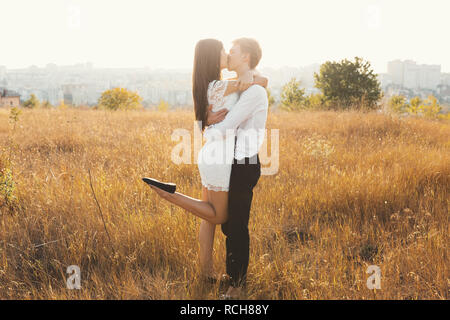 Loving couple dressed in white kissing outdoors, touching, gentle each other with a beautiful landscape in background, golden grass - Concept about pe Stock Photo