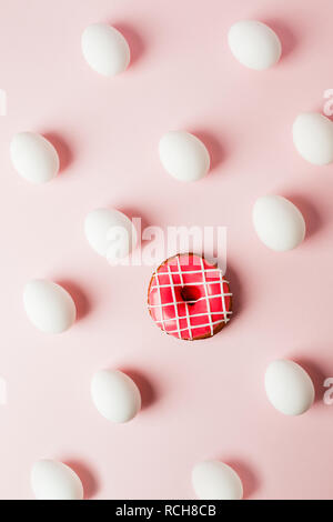 White eggs and pink donut on a light pink background with reflection of the shadows and copy space. layout to easter. Flat lay, pattern Stock Photo