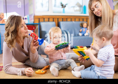 Nursery babies playing musical toys with teacher and assistant. Early musical education in kindergarten Stock Photo