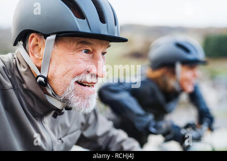 Active senior couple with electrobikes cycling outdoors on a road in nature. Stock Photo