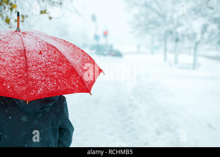 Woman under red umbrella in snow enjoying the first snowfall of the winter season Stock Photo