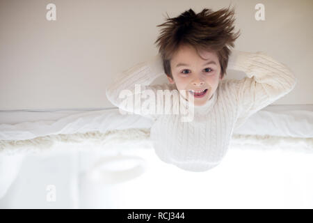 Cute portrait of child upside down, lying on bed, smiling at camera and playing with toy Stock Photo