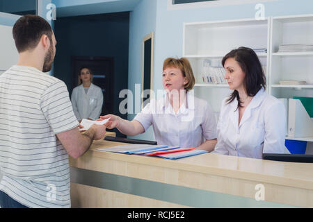 Qualified smiling doctors working with client at reception desk in hospital Stock Photo
