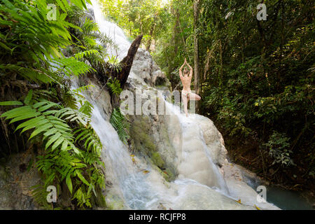Tropical yoga session by beautiful Sticky Waterfall close to Chiang Mai in north Thailand. Vriksha asana - tree pose. Stock Photo
