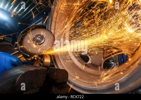 A close-up of a car mechanic using a metal grinder to cut   bearing in an auto repair shop, bright flashes flying in different directions. Work of aut Stock Photo