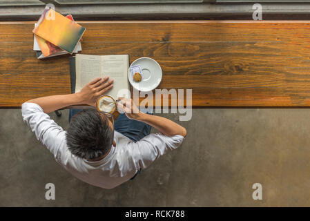 Young man drinking hot Cappuccino and reading book Stock Photo