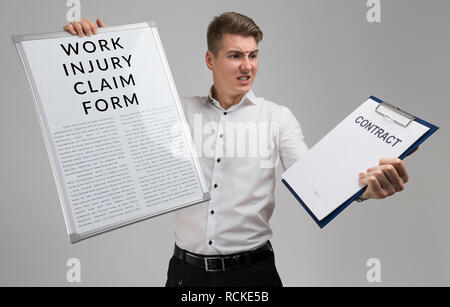 young man holding a form with a claim of injury at work and blank contract form isolated on a light background Stock Photo