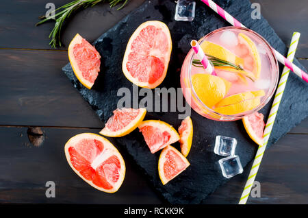 grapefruit juice or cocktail in glasses and pieces of grapefruit, ice cubes, straws on a dark background Stock Photo