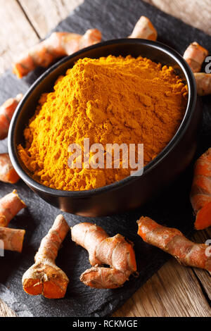 Ground fresh turmeric in a bowl and root close-up on the table. vertical Stock Photo