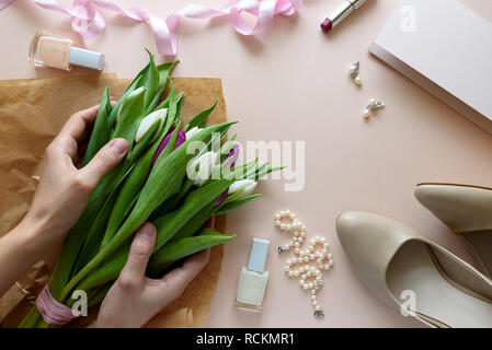 Hands holding bouquet of white and purple tulips. Feminine accessories and blank paper on pink background. Top view. Flat lay. Copy space. Valentines  Stock Photo