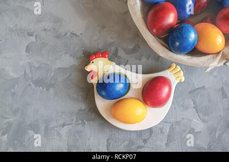 Multi-colored Easter eggs lie on a white plate in the shape of a chicken next to paint for coloring and Easter cakes. Copy space. Stock Photo
