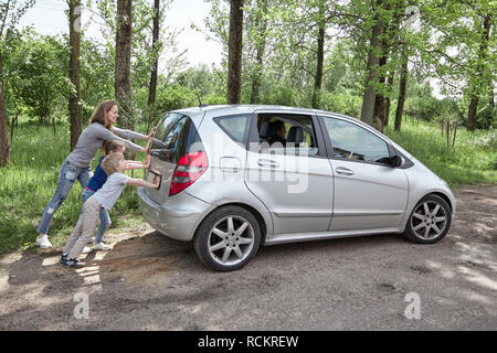 mom, son and daughter pushing a faulty car. Stock Photo