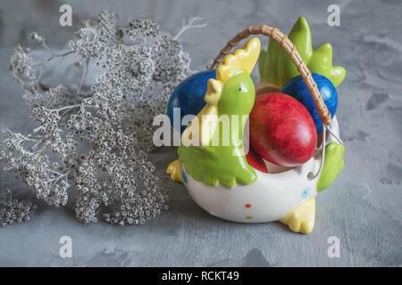 Multi-colored Easter eggs lie on a white plate in the shape of a chicken next to paint for coloring and Easter cakes. Copy space. Stock Photo