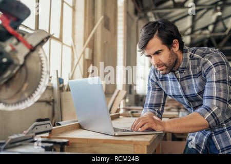 Woodworker doing research on a laptop in his workshop Stock Photo