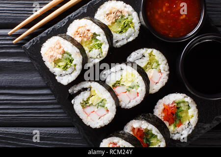 Set of japanese rolls futomaki with soy and chili sauces close-up on a slate board on the table. horizontal top view from above Stock Photo