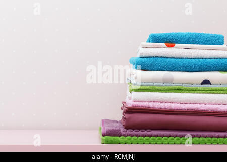 On the dresser there is a stack of clean ironed bed linen and folded colored towels. Stock Photo