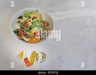Mixed green and purple salad with measuring tape on white marble table dieting fitness health conceptual background with shadow for copy space Stock Photo