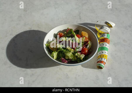 Mixed green and purple salad with measuring tape on white marble table dieting fitness health conceptual background with shadow for copy space Stock Photo