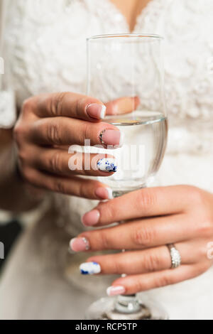 The girl sits on a soft bed, holding a glass with champagne in her hands. Wedding morning of the bride. 2019 Stock Photo