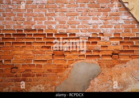 background image of old eroded plastered brick wall with most of the plaster and a lot of red brick missing Stock Photo