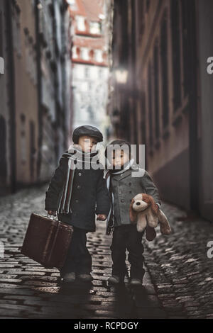 Two children, boy brothers, carrying suitcase and dog toy, travel in the city alone at night Stock Photo