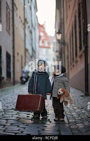 Two children, boy brothers, carrying suitcase and dog toy, travel in the city alone at night Stock Photo