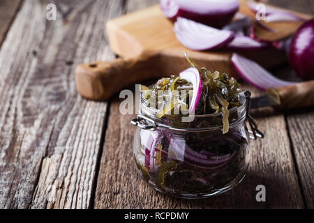 Pickled seaweed salad with red onion in glass jar, healthy sustainable food on rustic wooden table Stock Photo