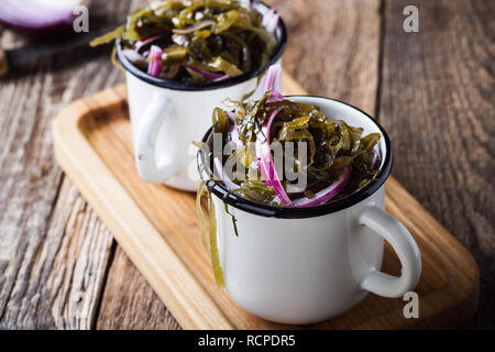 Pickled seaweed salad with red onion in rural mug, healthy sustainable food on rustic wooden table Stock Photo