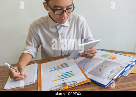 Man using tablet to check data and writing notes Stock Photo