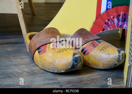 Old painted Dutch wooden clogs with a leather strap, on the floor of a tourist shop, next to a display stand. A bit of display stand shows. Stock Photo