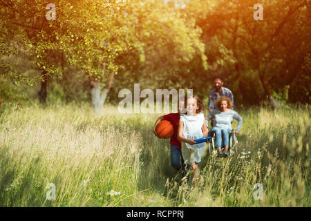 Children ran and laugh while their mother on wheelchair and father are running after them Stock Photo