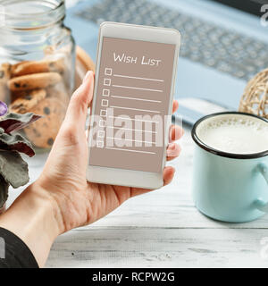 Woman hand using cell phone sitting on the table with laptop, cookies and milk for virtual Santa. Digital Christmas Wish List concept Stock Photo