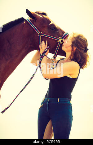 Taking care of animals, love and friendship concept. Jockey young girl kissing and hugging brown horse on sunny day Stock Photo