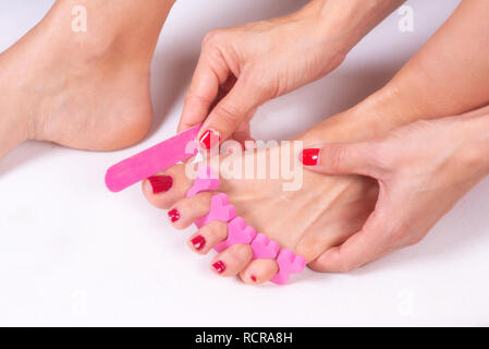 applying pedicure to woman's feet with red toenails, in pink toe separators . Stock Photo