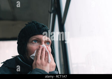 Woman blowing her nose into paper handkerchief on the bus on a cold winter day at the start of the flu season
