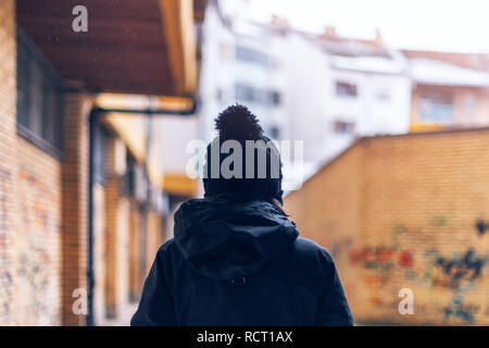 Rear view of casual adult woman walking on urban city street during the light snowfall in winter Stock Photo