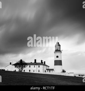 A wet & windy winter sunrise, a brief glimse of the sun lights up the clouds before dark storm clouds quickly follow engulfing the lighthouse Stock Photo