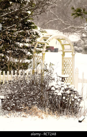 Garden after snowstorm including one with tall birdhouse and another with trellis and fence. Stock Photo